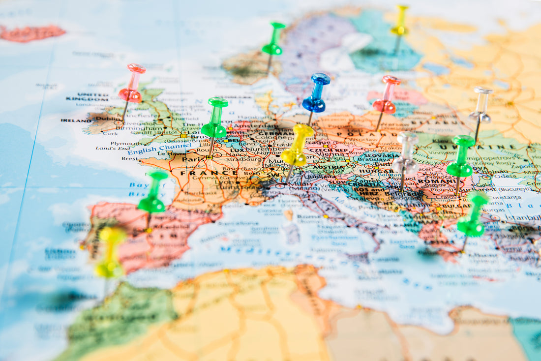 Front-angled overhead view of a colorful map of Europe with several pins stuck into it to mark different travel destinations