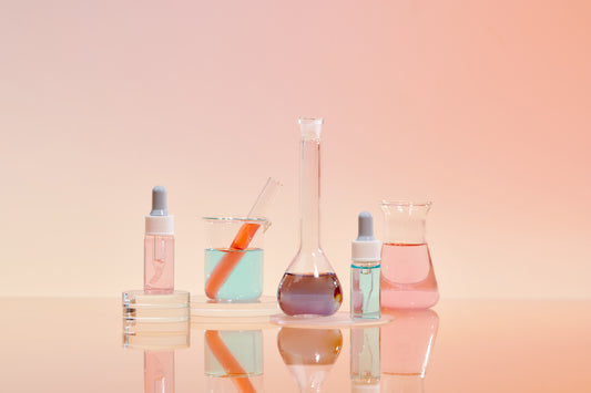 Chemistry flasks, tincture bottles, beakers, and a test tube with different colored liquids inside shown on a glowing pink lighted surface
