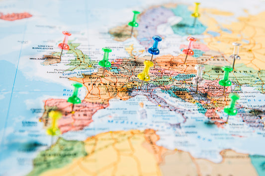 Front-angled overhead view of a colorful map of Europe with several pins stuck into it to mark different travel destinations